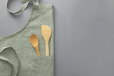 Clean apron with wooden kitchen tools on light grey background, top view. Space for text