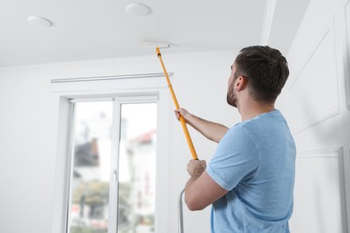 Young man painting ceiling with white dye indoors, space for text