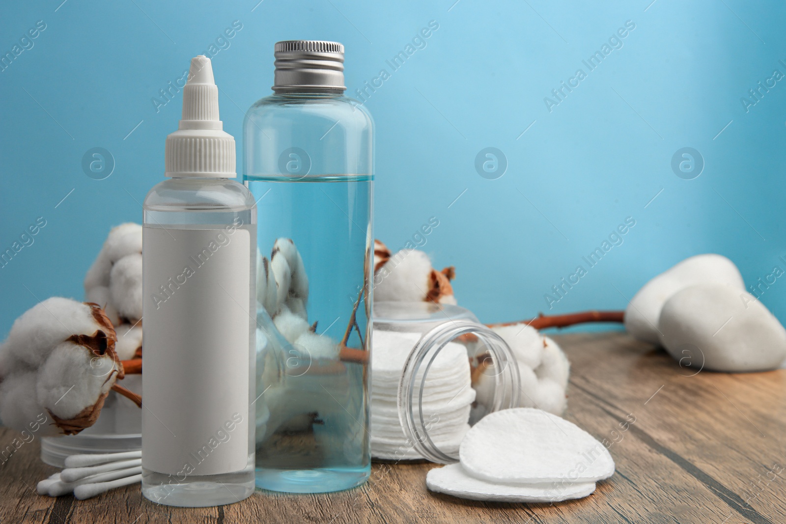 Photo of Composition with makeup removers and cotton flowers on wooden table against light blue background