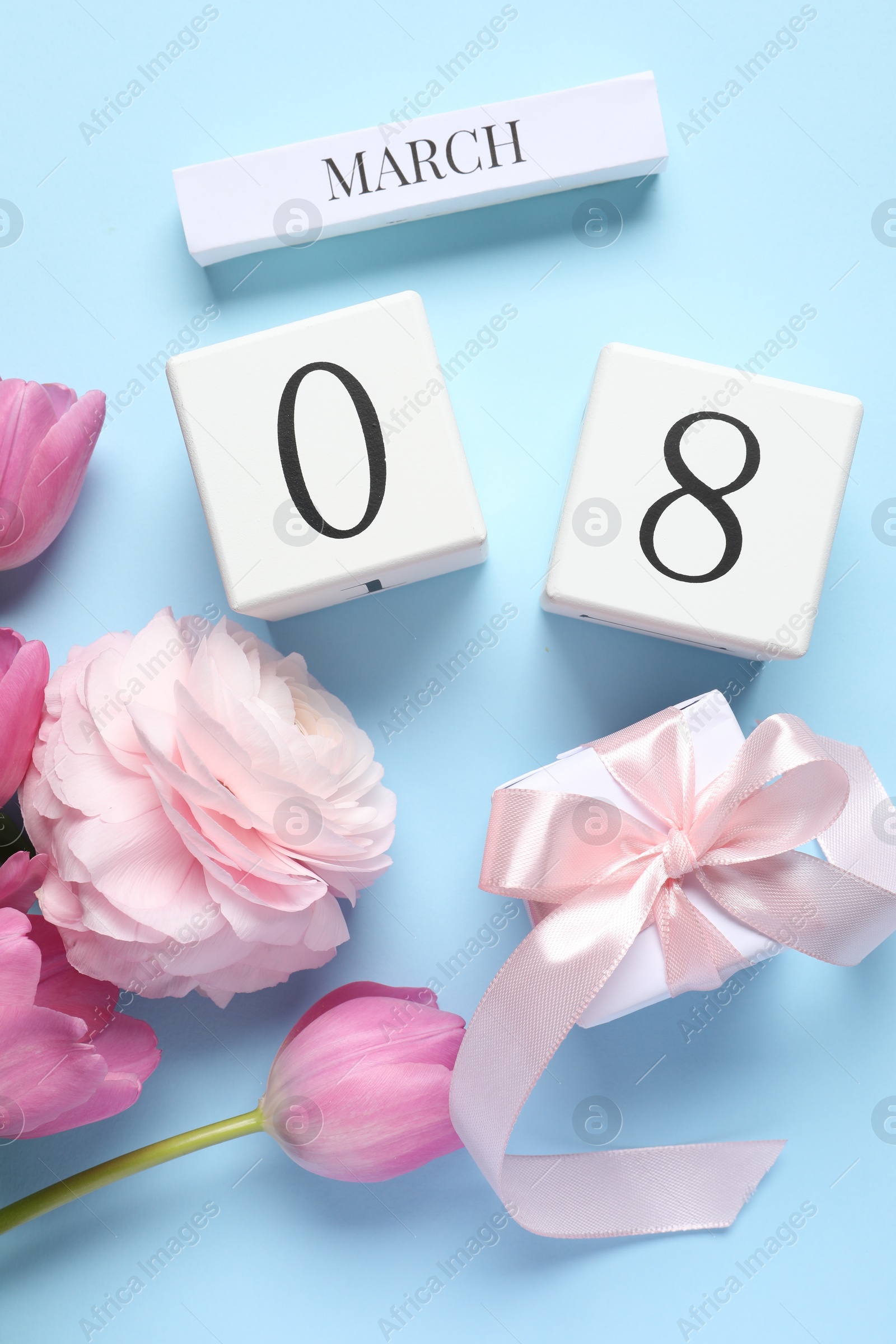 Photo of International Women's day - 8th of March. Gift box, wooden block calendar and beautiful flowers on light blue background, flat lay