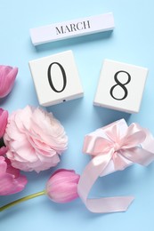 Photo of International Women's day - 8th of March. Gift box, wooden block calendar and beautiful flowers on light blue background, flat lay