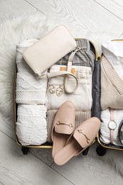 Open suitcase with folded clothes, shoes and accessories on floor, top view