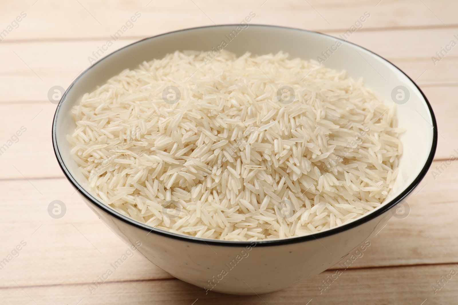 Photo of Raw basmati rice in bowl on white wooden table, closeup