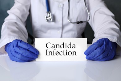Doctor holding card with phrase Candida Infection at white table, closeup
