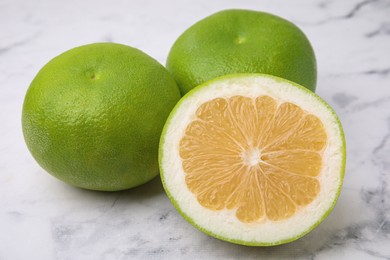 Photo of Whole and cut sweetie fruits on white marble table, closeup