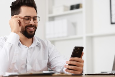 Photo of Handsome young man using smartphone at table in office