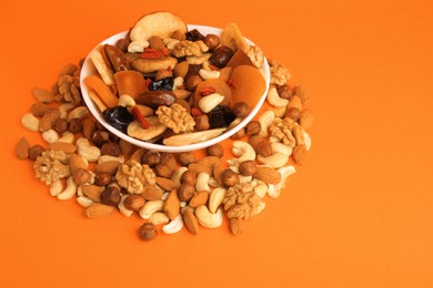 Bowl with mixed dried fruits and nuts on orange background, space for text