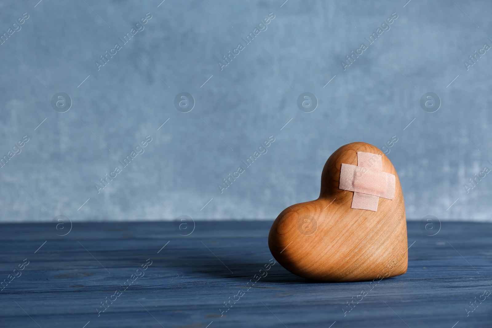 Photo of Wooden heart with adhesive plasters on table. Space for text