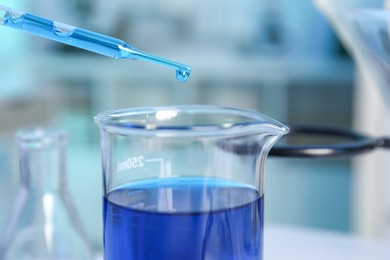 Photo of Laboratory analysis. Dripping blue liquid into beaker on table, closeup