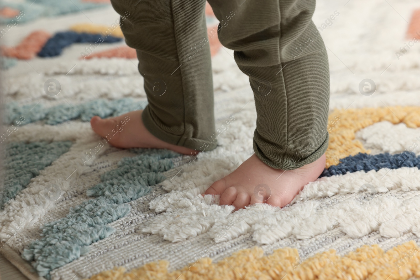 Photo of Baby standing on soft colorful carpet, closeup