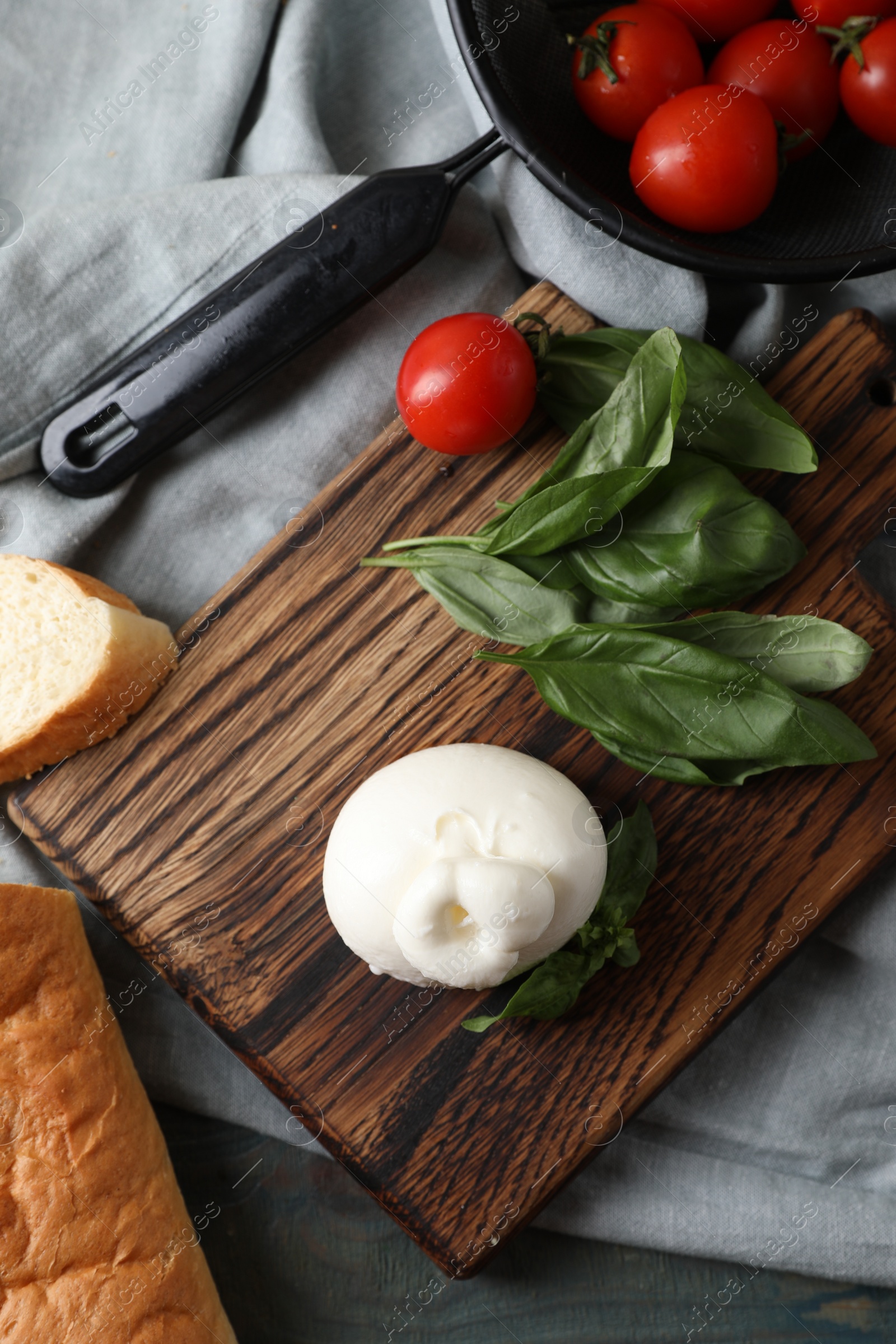 Photo of Delicious burrata cheese with basil and tomatoes on grey wooden table, top view