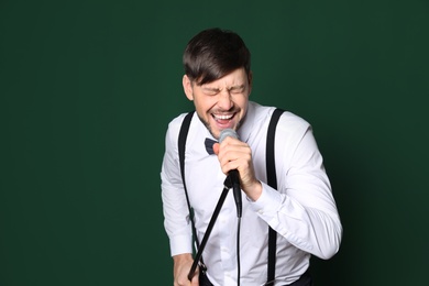 Handsome man in formal clothes singing with microphone on color background