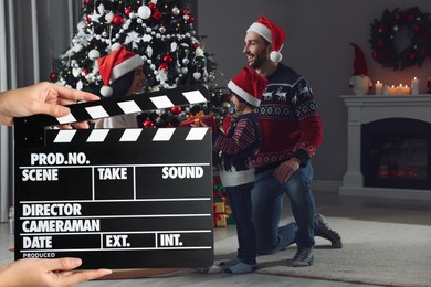 Shooting movie. Second assistant camera holding clapperboard in front of happy family celebrating Christmas (actors) at home (film set)