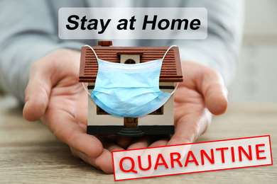 Image of Stay at home during coronavirus quarantine. Man holding house model with medical mask