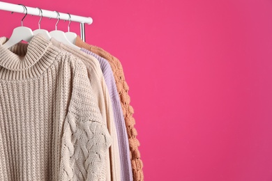 Collection of warm sweaters hanging on rack against color background. Space for text