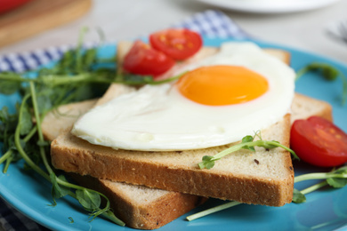 Photo of Tasty fried egg with bread and garnish on blue plate, closeup