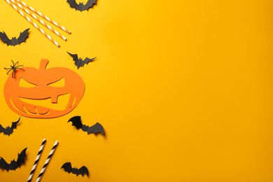 Photo of Flat lay composition with spooky paper pumpkin, bats and straws on yellow background, space for text. Halloween celebration