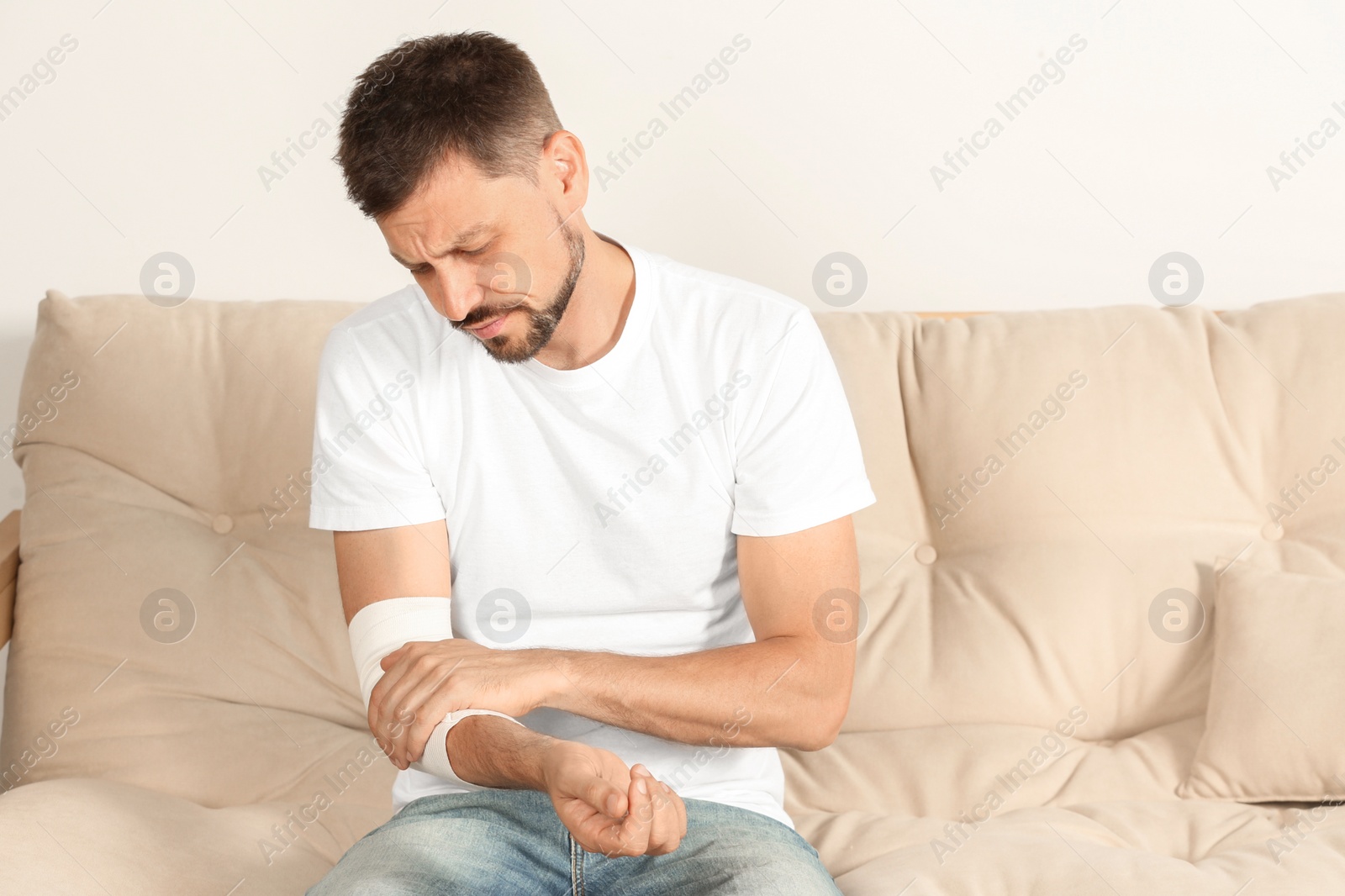 Photo of Man with arm wrapped in medical bandage on sofa indoors