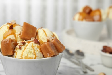 Photo of Delicious ice cream served with caramel and hazelnuts on marble table, closeup. Space for text