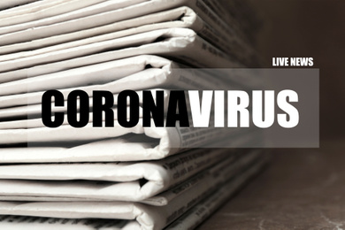 Image of Word CORONAVIRUS and stack of newspapers on table, closeup. Journalist's work