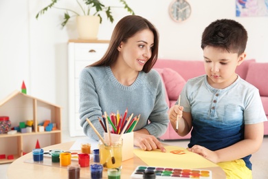 Photo of Cute little child painting at table with young mother in playing room