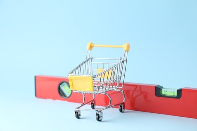 Photo of Measure level and empty shopping cart on light blue background