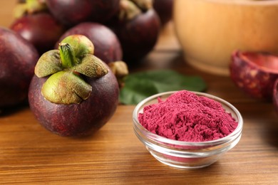 Photo of Purple mangosteen powder and fruits on wooden table, closeup