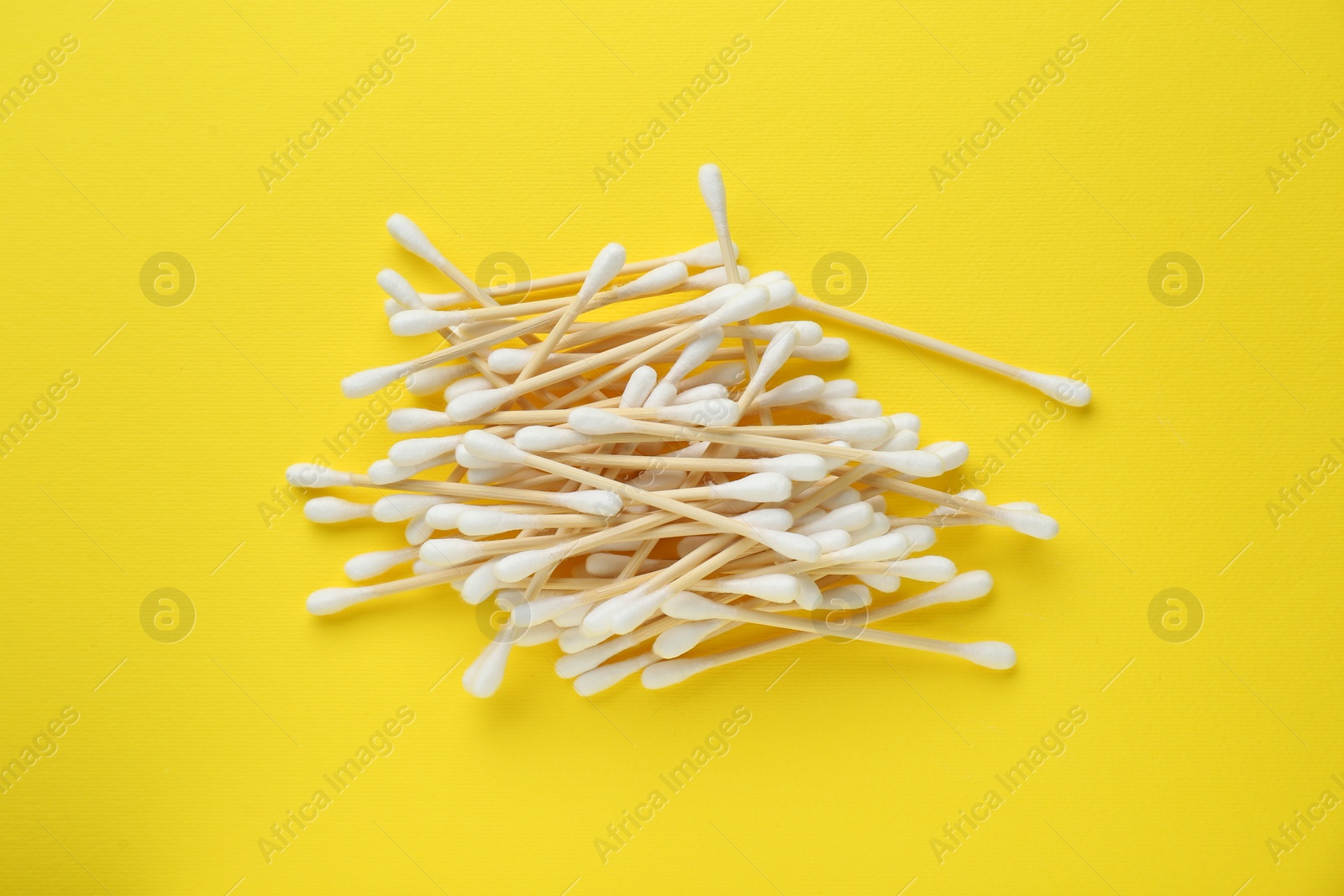 Photo of Heap of wooden cotton buds on yellow background, flat lay