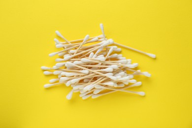 Photo of Heap of wooden cotton buds on yellow background, flat lay