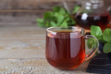 Photo of Cup with hot aromatic mint tea on wooden table. Space for text