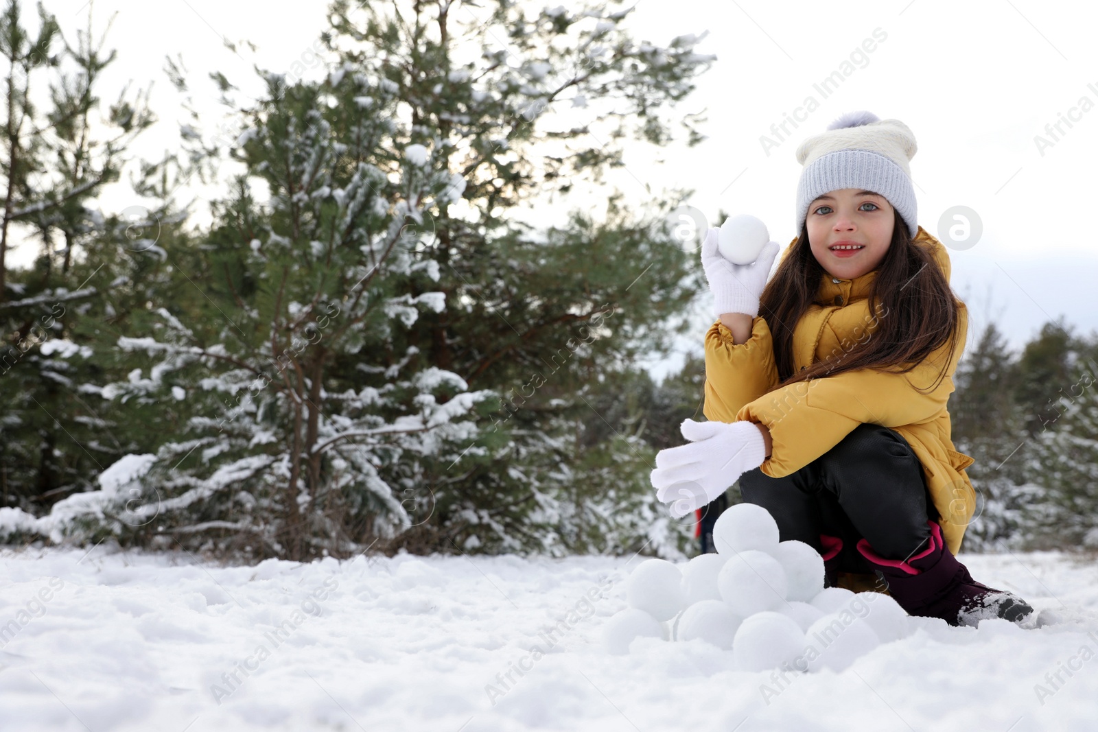 Photo of Cute little girl rolling snowballs in winter forest