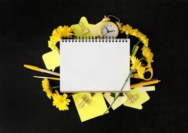 Photo of Different school stationery, blank notebook and beautiful yellow flowers on blackboard, flat lay with space for text. Happy Teacher's Day