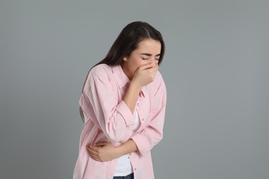 Young woman suffering from stomach ache and nausea on grey background. Food poisoning