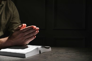 Religion. Christian man praying over Bible at table against black background, closeup. Space for text