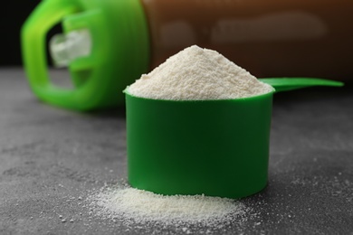 Photo of Measuring scoop of protein powder on grey stone table, closeup