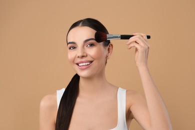 Beautiful woman applying makeup on light brown background