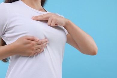 Woman doing breast self-examination on light blue background, closeup