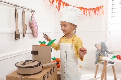 Little girl playing with toy cardboard kitchen at home
