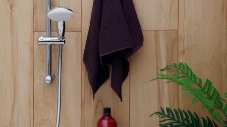 Photo of Brown soft towel near showerhead on tiled wall in bathroom