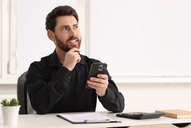 Photo of Smiling man with smartphone at table in office. Space for text