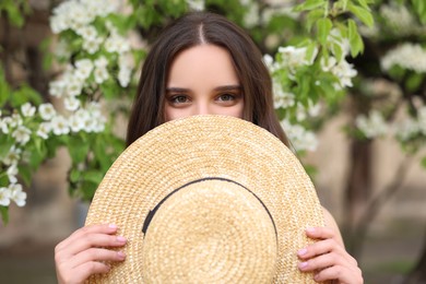 Beautiful woman with straw hat near blossoming tree on spring day