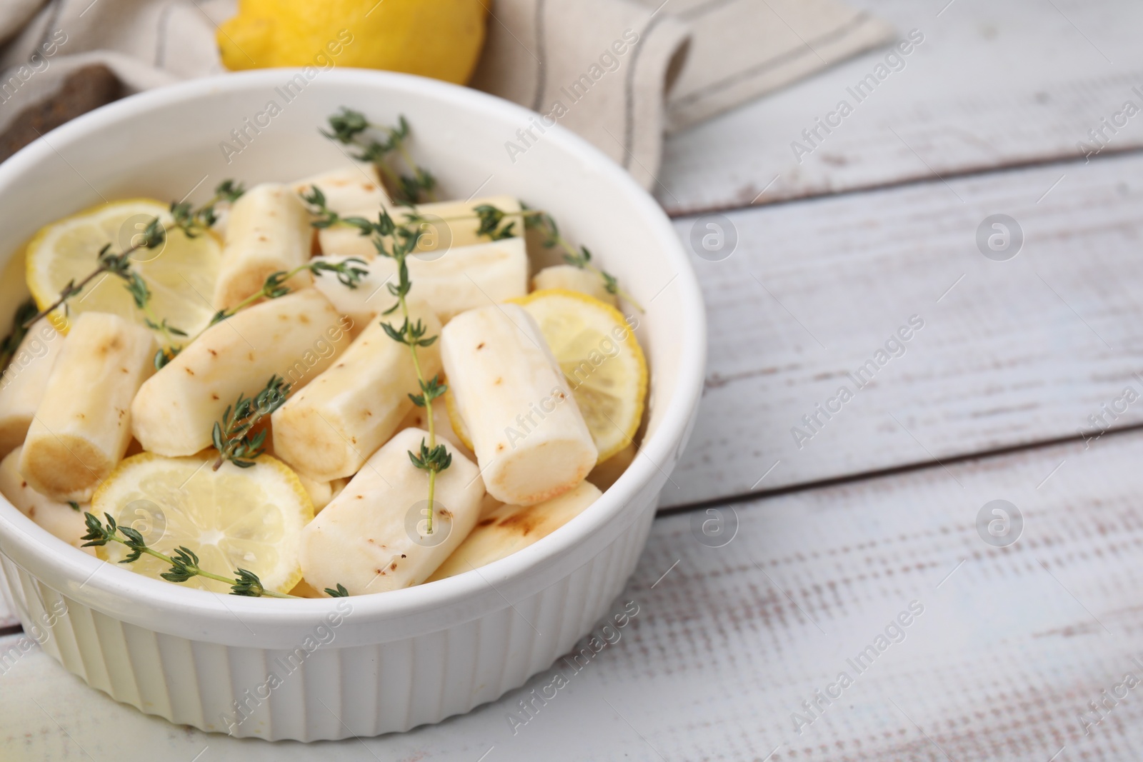 Photo of Dish with raw salsify roots, lemon and thyme on white wooden table, closeup. Space for text