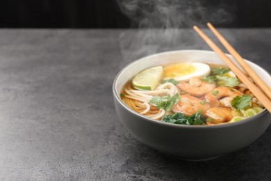 Image of Delicious hot ramen with shrimps and chopsticks on grey table, closeup with space for text. Noodle soup