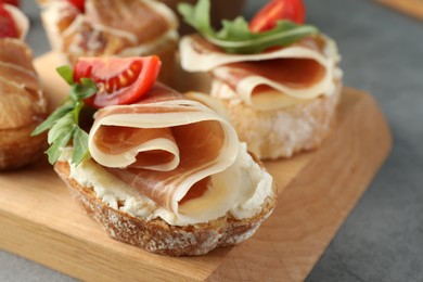 Photo of Tasty sandwiches with cured ham, tomatoes and arugula on grey table, closeup