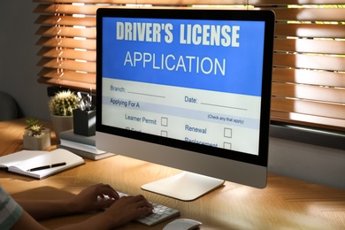 Photo of Woman using computer to fill driver's license application form at table in office, closeup