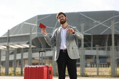 Being late. Worried businessman with red suitcase and passport outdoors