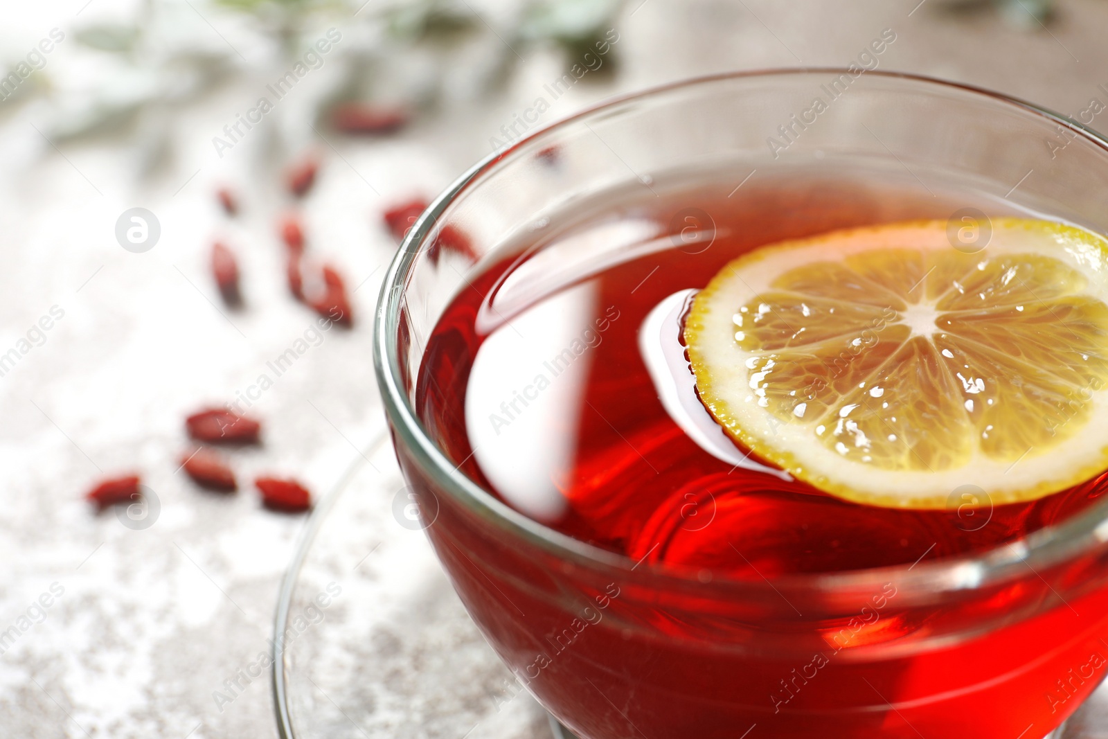 Photo of Glass cup of healthy goji tea with lemon on beige table, closeup. Space for text