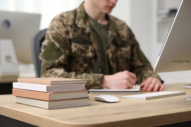 Photo of Military education. Student in soldier uniform learning at wooden table indoors, selective focus