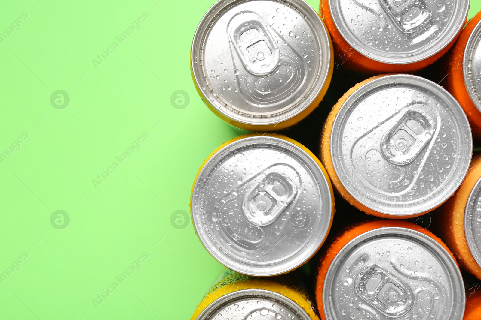 Photo of Energy drinks in wet cans on green background, top view. Space for text