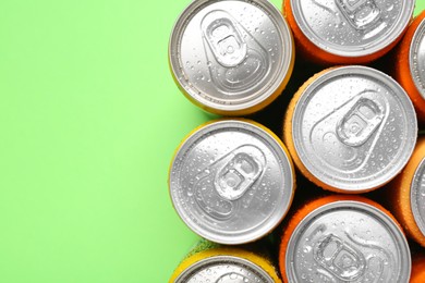 Energy drinks in wet cans on green background, top view. Space for text